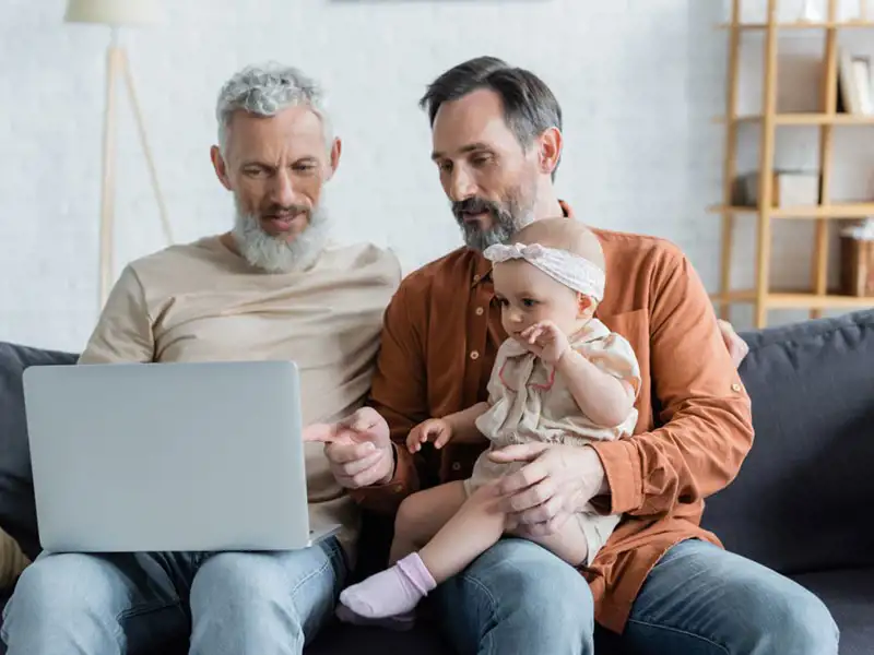 Two older men holding a baby while looking at a computer
