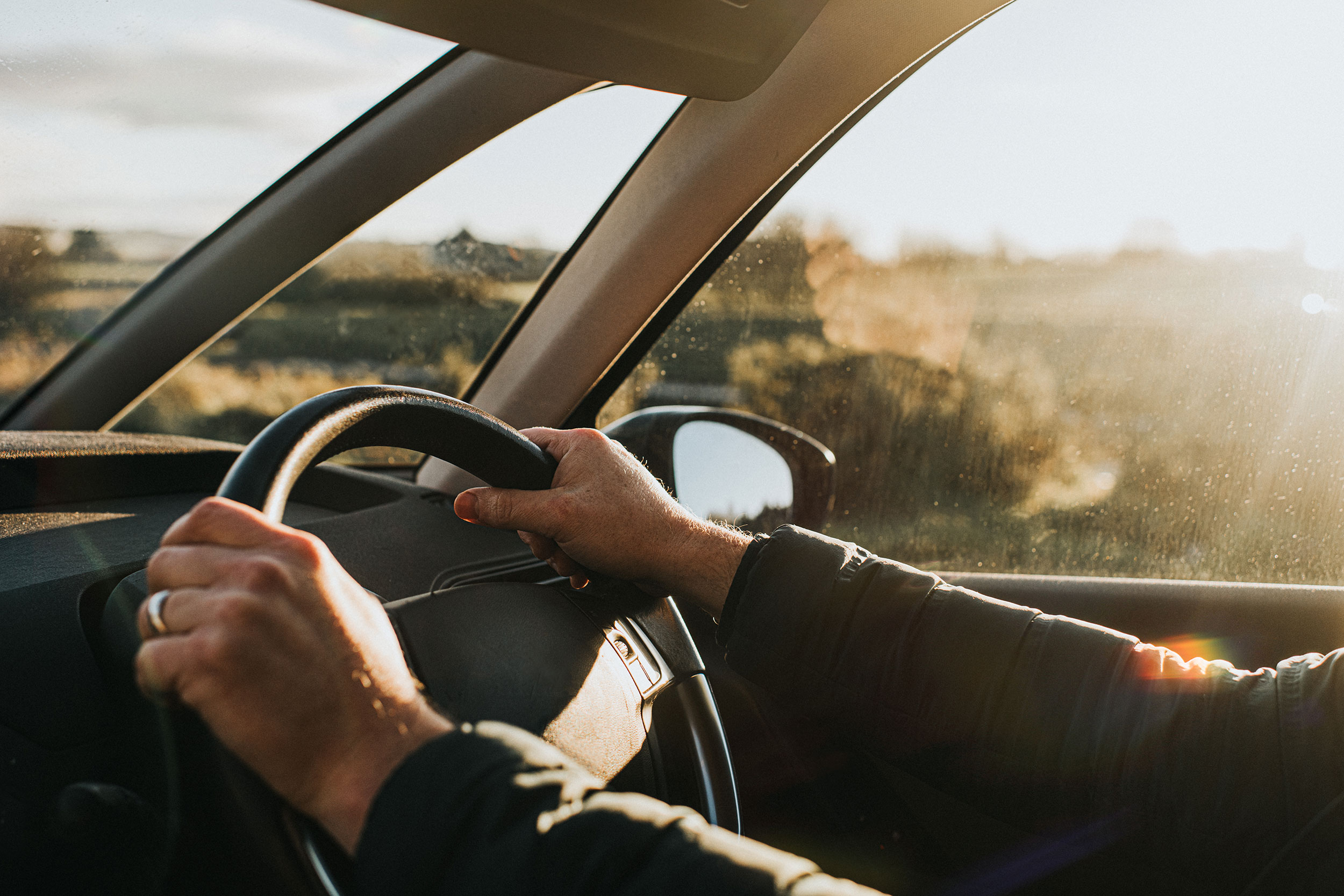 Hands hold the steering wheel of a vehicle as late afternoon sunlight floods in