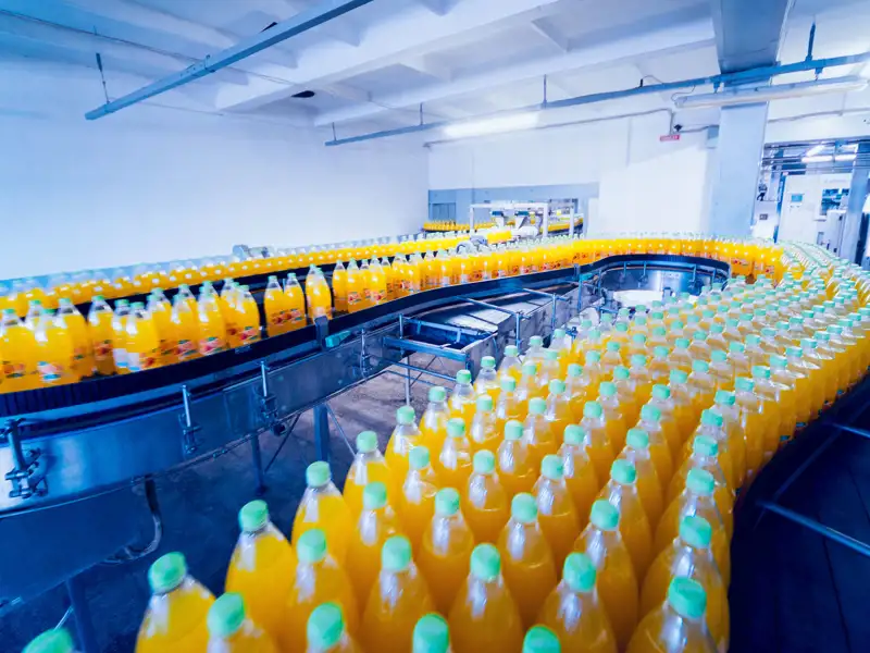 Bottles of an orange drink travel along an assembly line