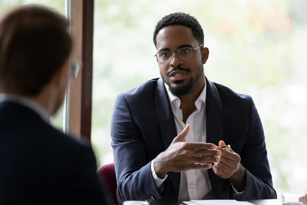 A man at a desk is giving an explanation to other person