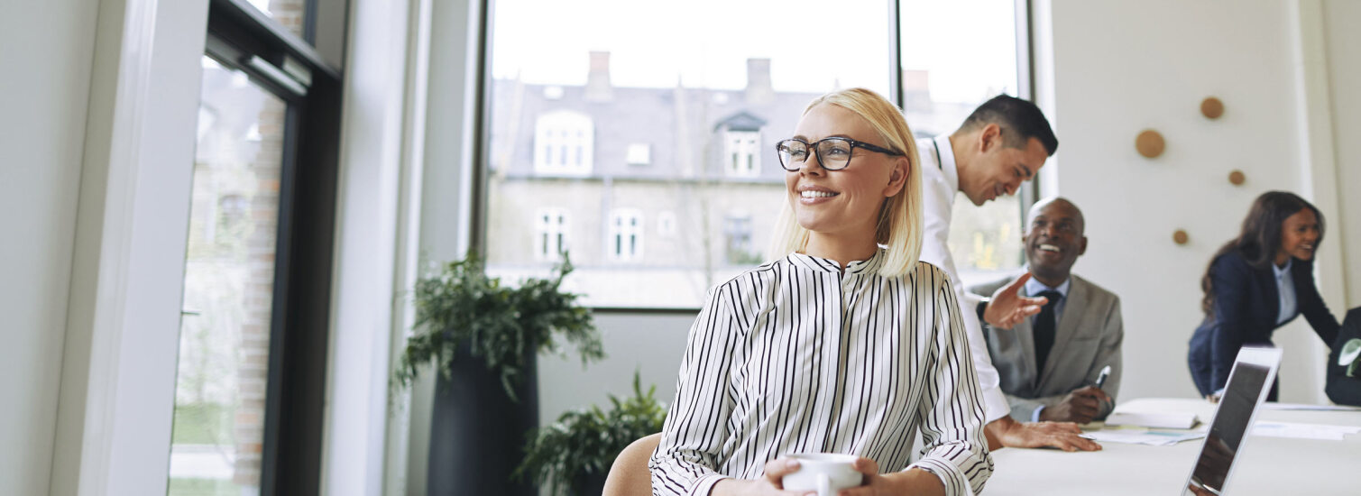 Smiling young businesswoman enjoying her coffee during an office break.